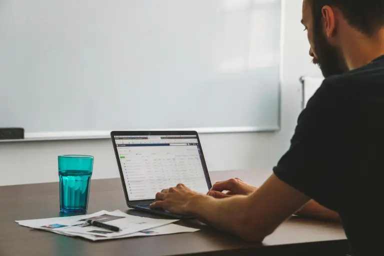 homme travaillant sur laptop avec données analytiques, verre d'eau et documents sur bureau