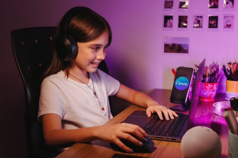 A smiling young girl wearing headphones using a laptop for creative activities, indoors.
