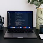 Laptop displaying code next to a lucky cat statue.