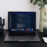 Laptop displaying code next to a lucky cat statue.